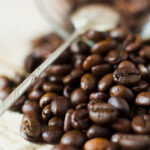 Grains of roasted Arabica coffee with a metal spoon on a background of wooden planks, natural light.