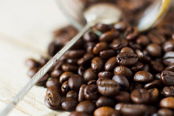 Grains of roasted Arabica coffee with a metal spoon on a background of wooden planks, natural light.